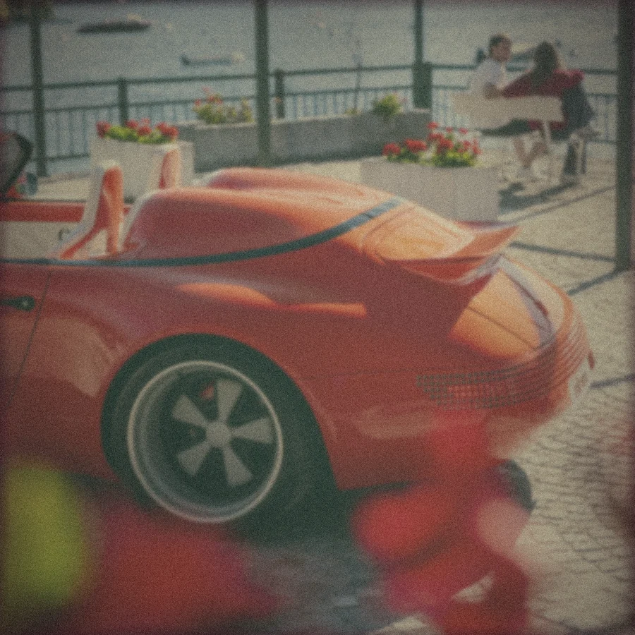 Polaroid: the Funkster’s tail on a lakeside terrace, geraniums in front and a couple on a bench behind